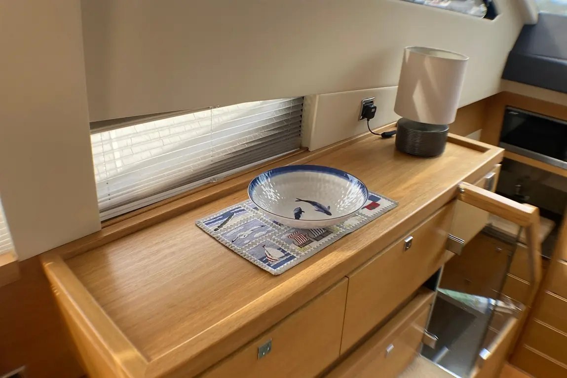 Modern boat interior featuring a wooden counter, a decorative bowl, a lamp, and patterned placemat near a window.
