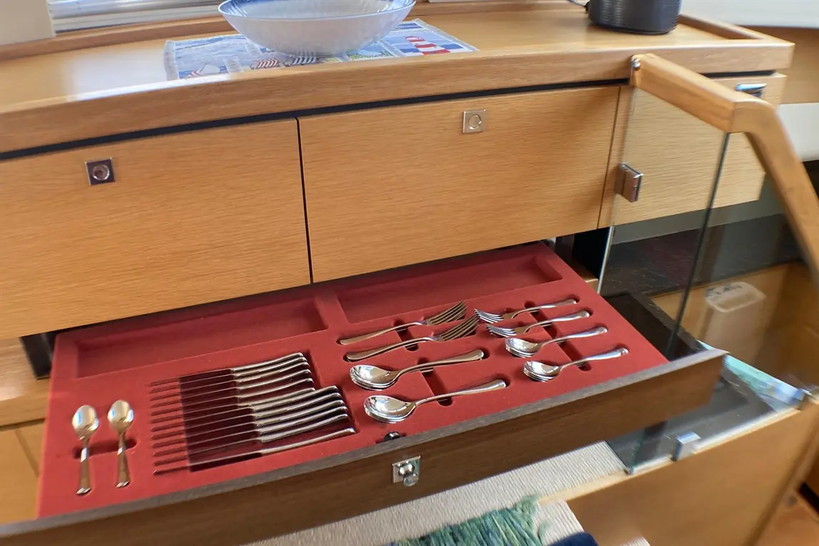 Drawers containing organised silver cutlery on a red velvet tray, complemented by a bowl on a wooden surface.