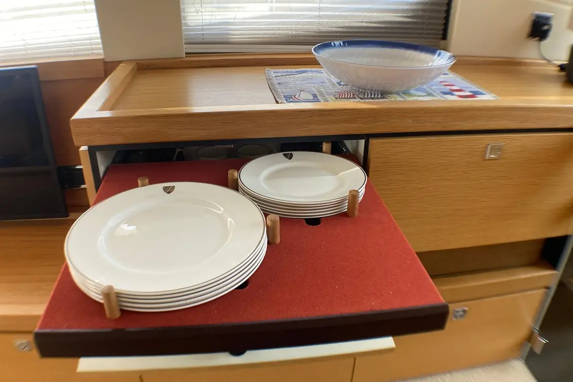 White plates stacked on a red velvet mat in a kitchen drawer, with a large bowl on a wooden countertop beside them.