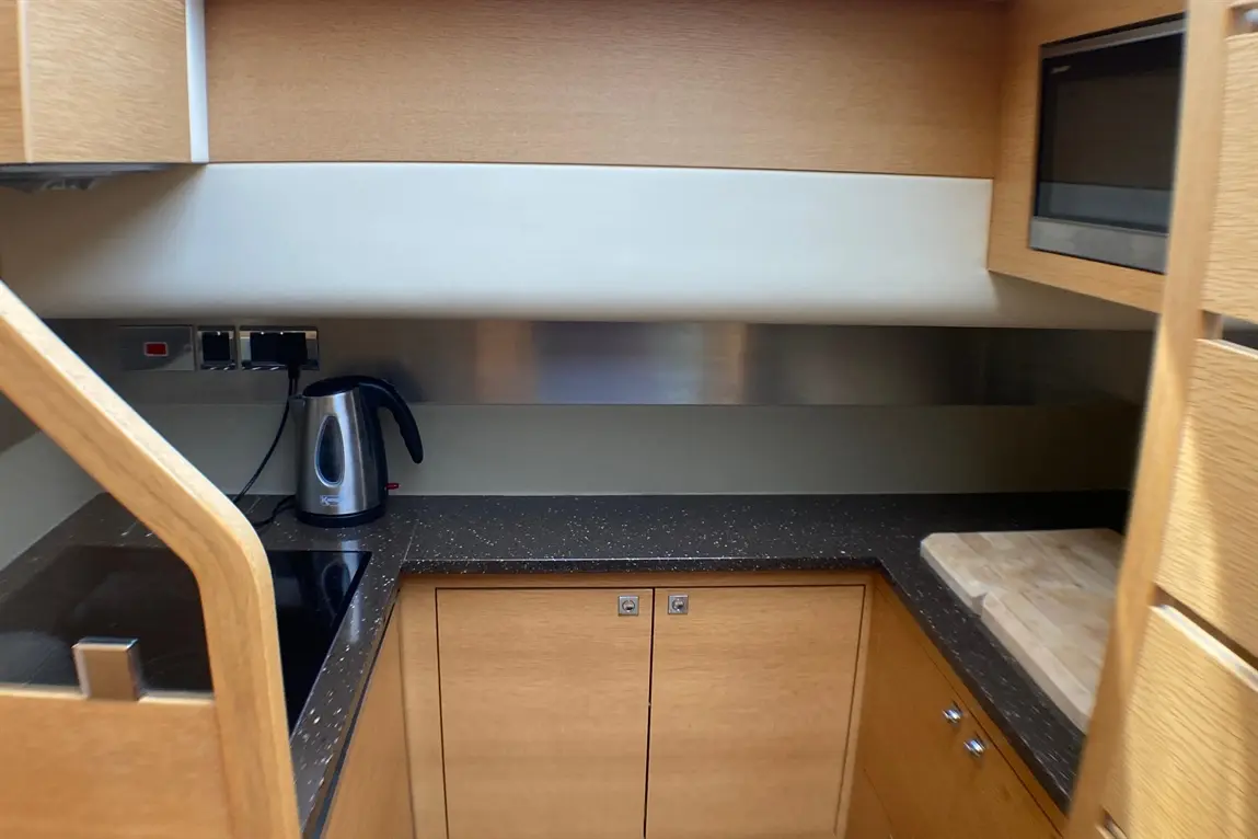 Modern kitchen interior with a kettle, induction hob, stainless steel backsplash, and wooden cabinets.