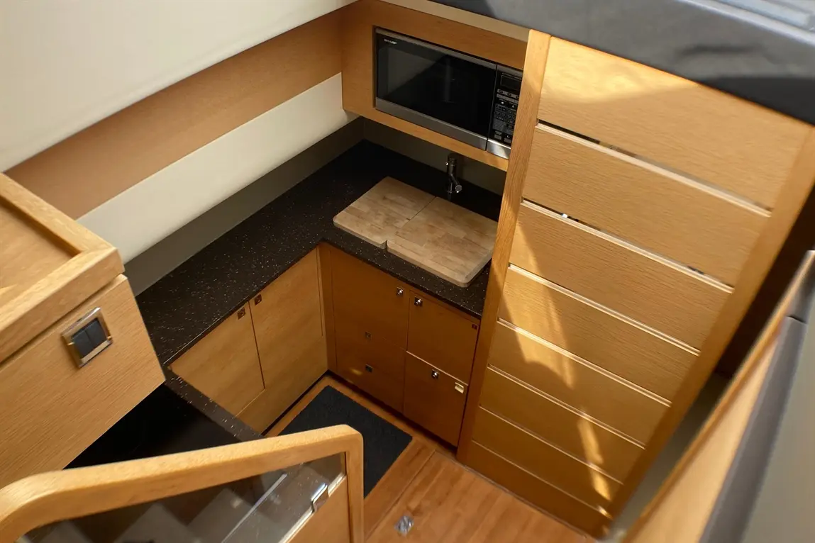 Modern boat kitchen featuring wooden cabinets, a microwave, a dark countertop, and a wooden chopping board.