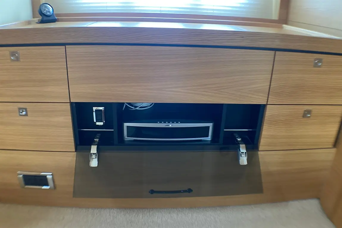 Wooden cabinetry with a glossy drawer, containing a sound system and cables, beside a clock on the surface.