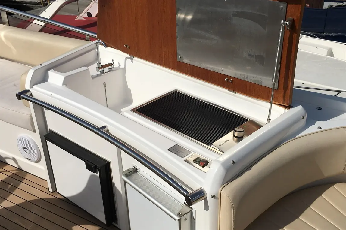 Outdoor boat kitchenette with a grill, sink, and storage cabinets, featuring stainless steel accents and a wooden backdrop.