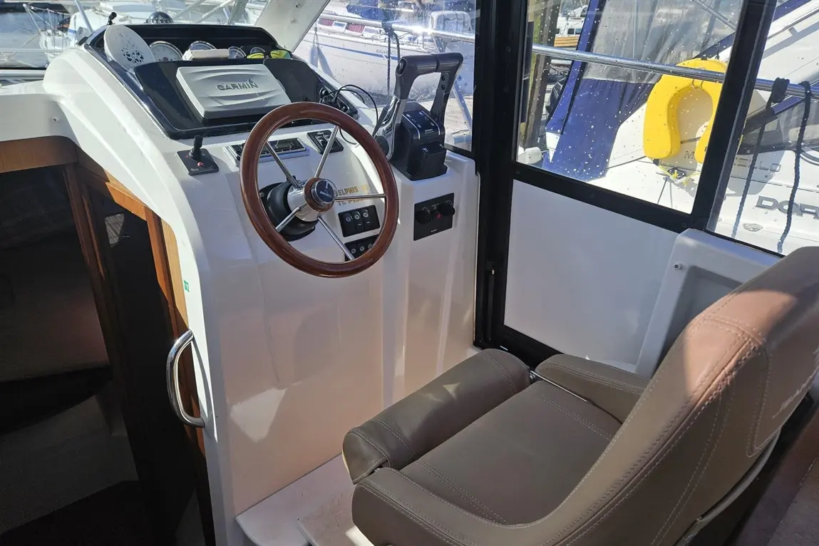 Boat cockpit featuring a wooden steering wheel, throttle controls, and a captain's seat, with views of other boats outside.