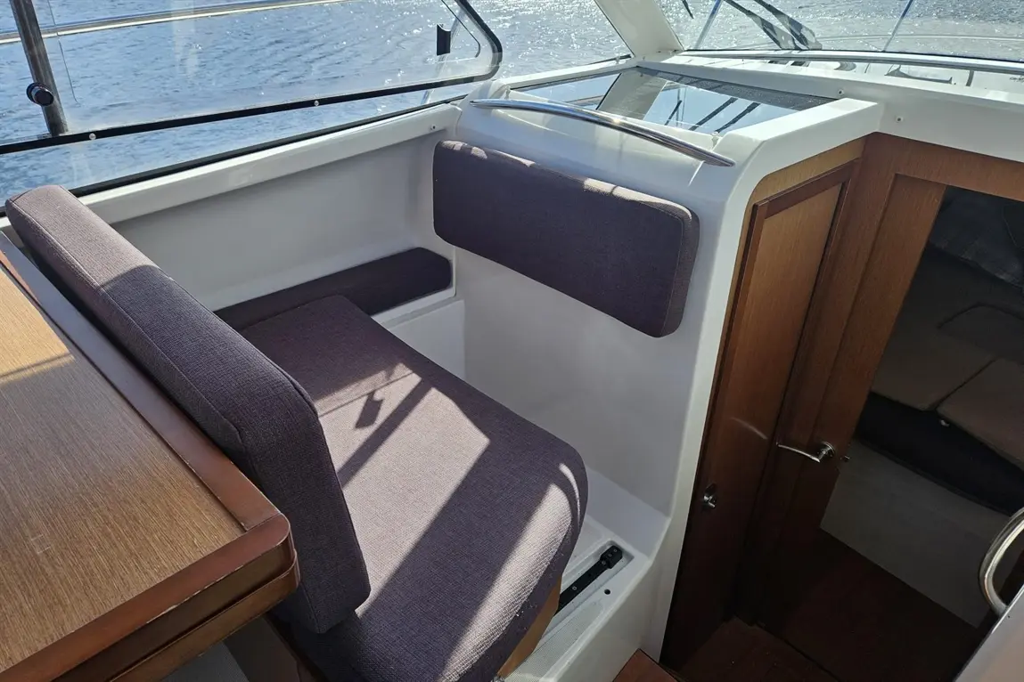 Boat interior featuring a modern seating area with a plush seat and wooden table, sunlight streaming in over the water.