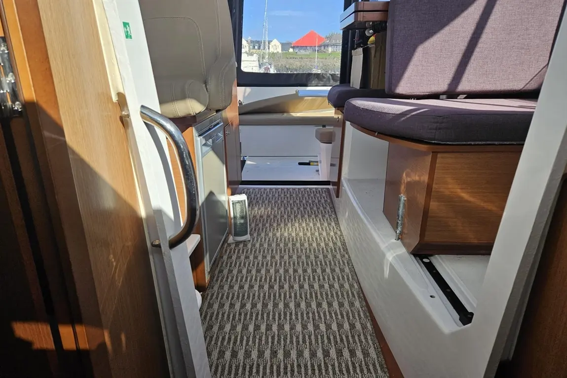 Interior of a boat showcasing a hallway with a textured rug, leather seating, and visible cooler beneath the counter.