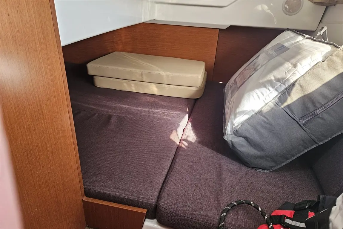 Interior of a boat cabin featuring a brown wooden panel, dark purple cushions, and a beige foam mattress on top.