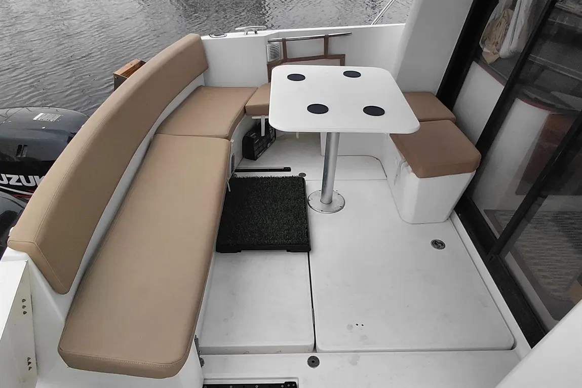 Seating area on a boat featuring beige cushions, a white table with four black cup holders, and a small artificial grass mat.