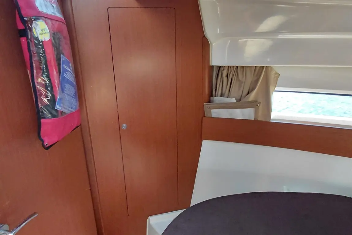 Interior of a boat showing wooden walls, a closed cupboard, and a pocket containing documents, with a view of water outside.