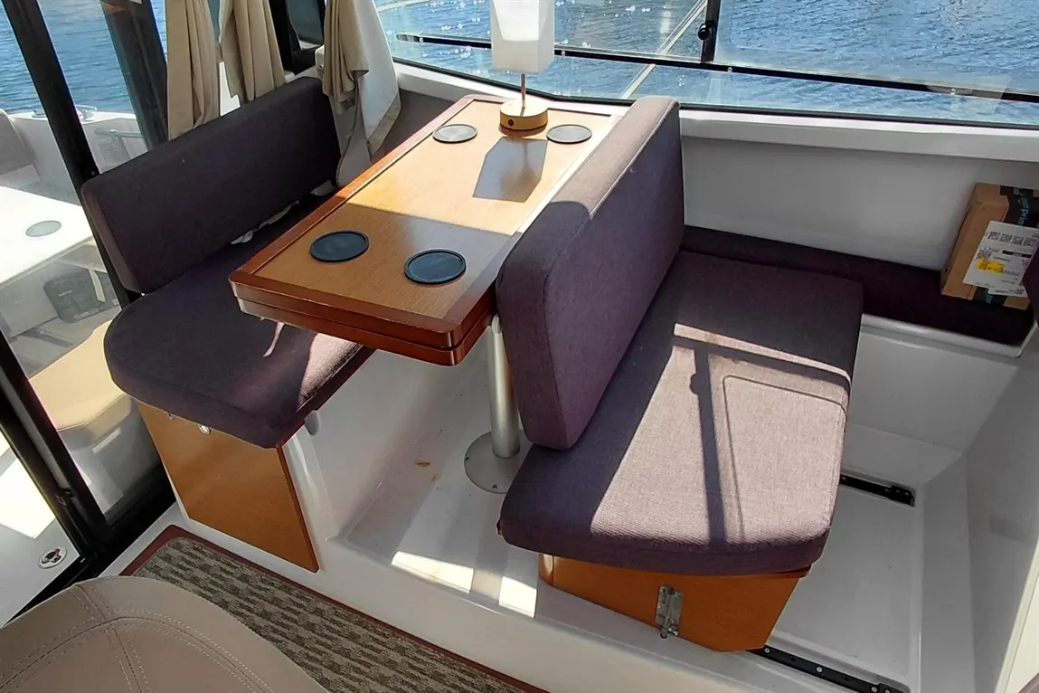 Interior of a boat featuring a wooden table, purple upholstered seating, and a sunlit view of water outside.