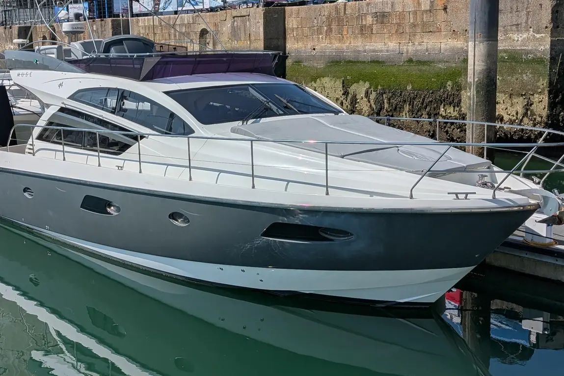 A stylish motorboat docked at a marina, featuring a sleek grey and white design and reflecting in the water.