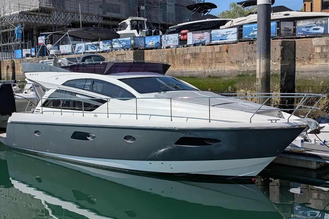 Luxury motorboat docked at a marina, with reflections visible in the water and construction in the background.