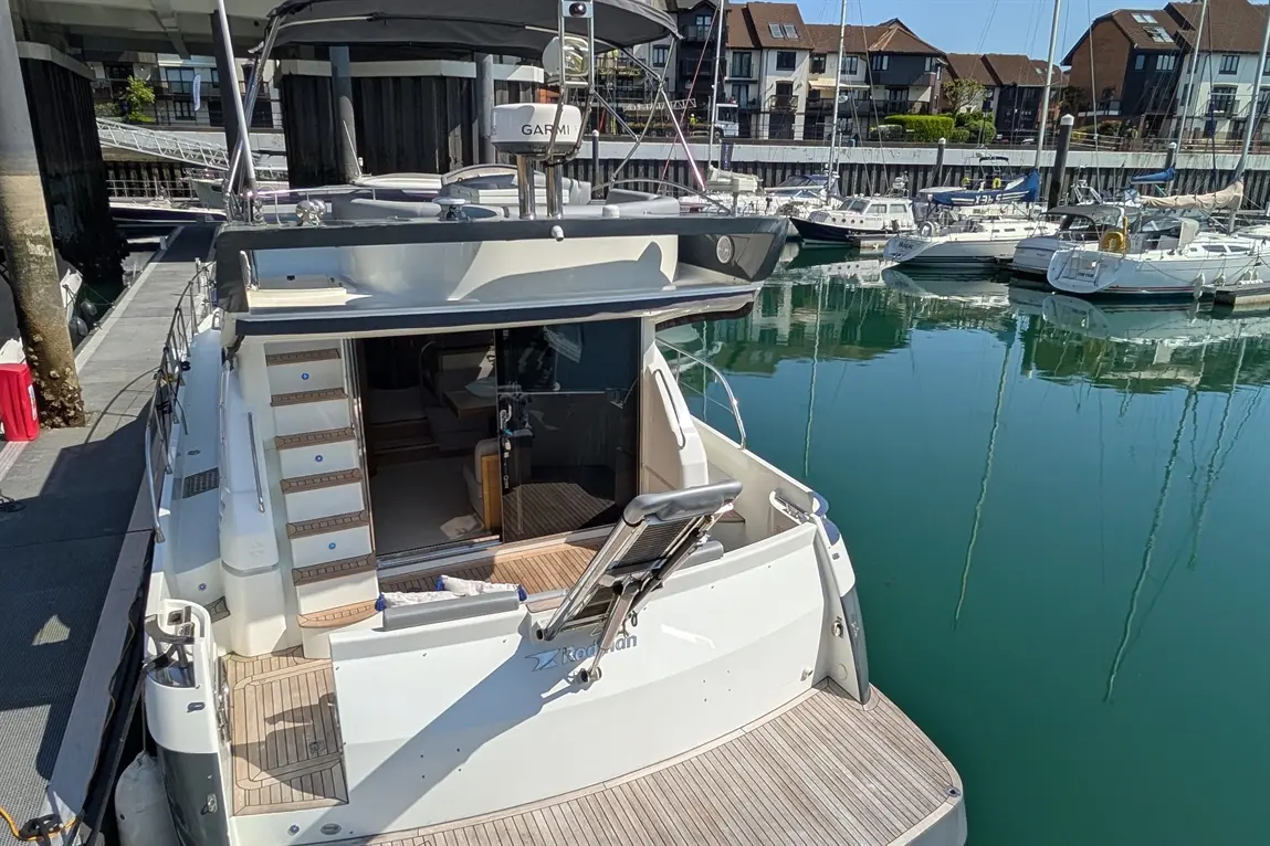 A sleek motorboat docked at a marina, featuring steps, a helm, and surrounding boats reflected in calm water.