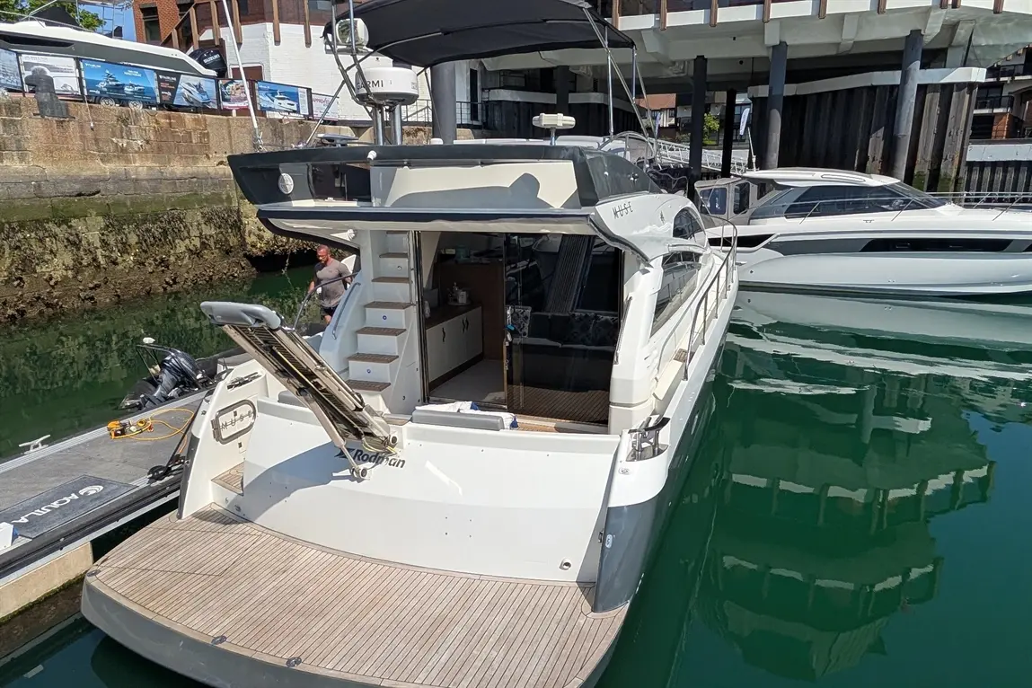 Luxury motorboat moored at a marina, with a man washing the deck and stylish interior visible through the cabin.