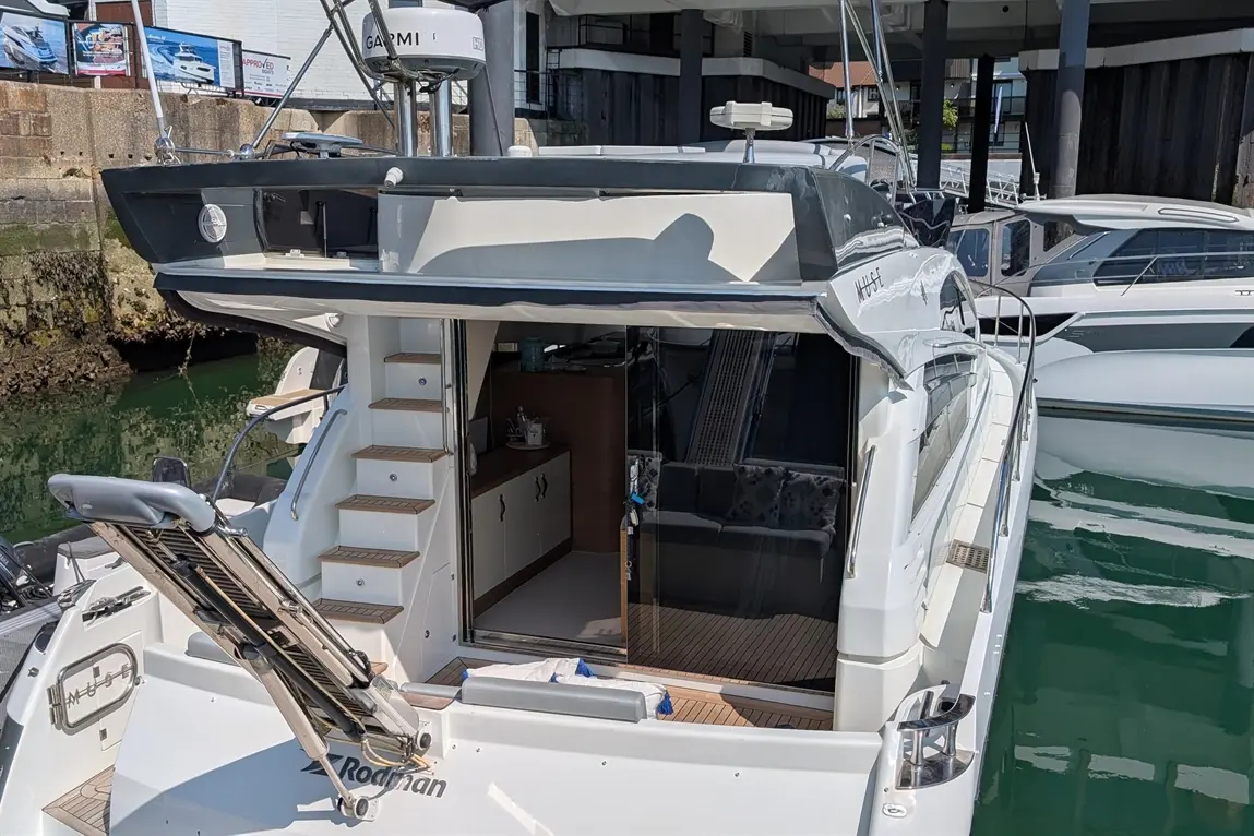 A luxury motorboat docked, featuring steps, a spacious deck, and a modern interior visible through glass doors.