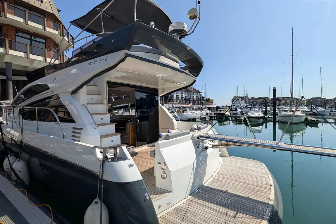 Luxury yacht "Muse" docked at a marina, with clear blue skies and numerous boats reflected in the water.