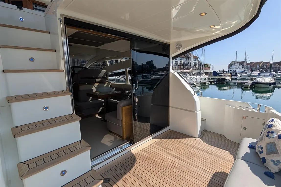 A luxurious yacht deck features steps leading to an interior with nautical views, furniture, and boats in the marina.