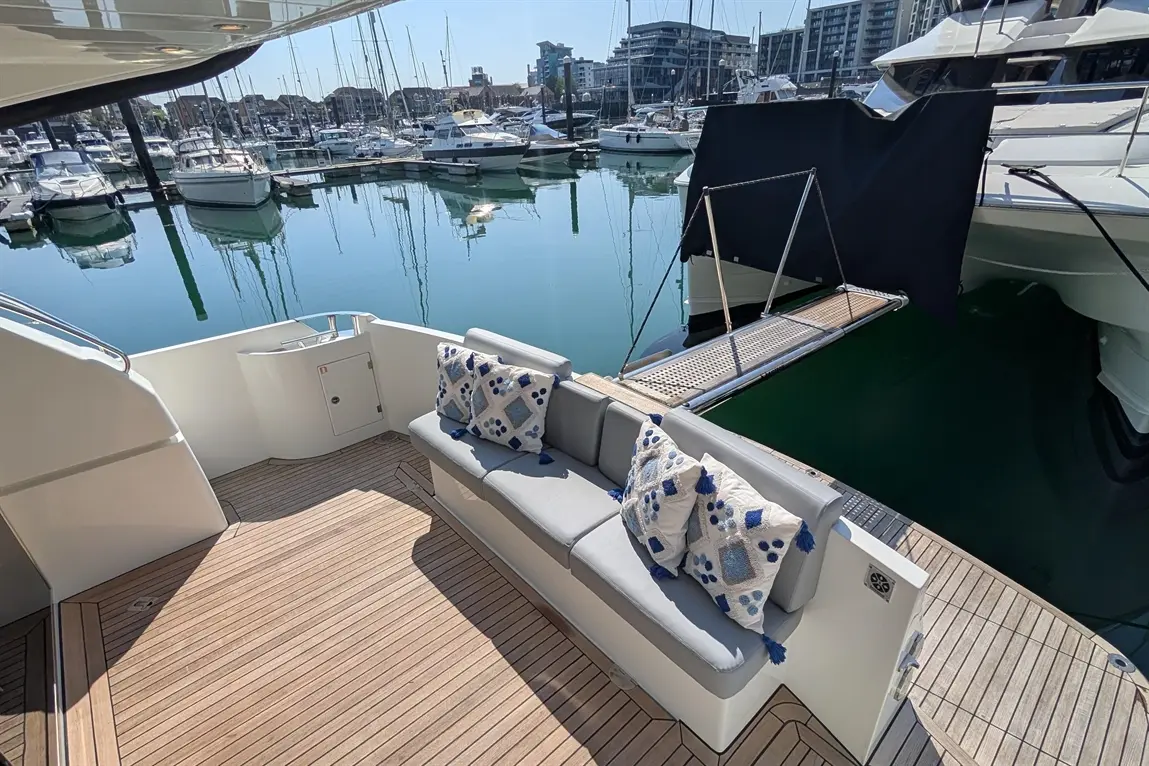 Luxury yacht exterior with plush seating, decorative cushions, and a view of the marina and boats in calm water.