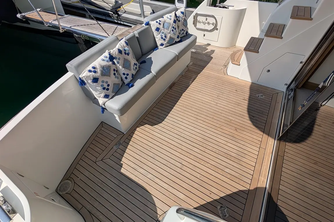 Stylish yacht deck with grey seating, decorative cushions, and wooden flooring under bright sunlight.