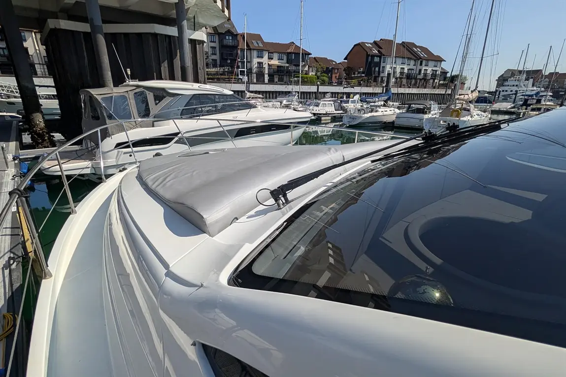 A close-up view of a white boat's bow with a grey cover, moored in a marina surrounded by other boats and buildings.