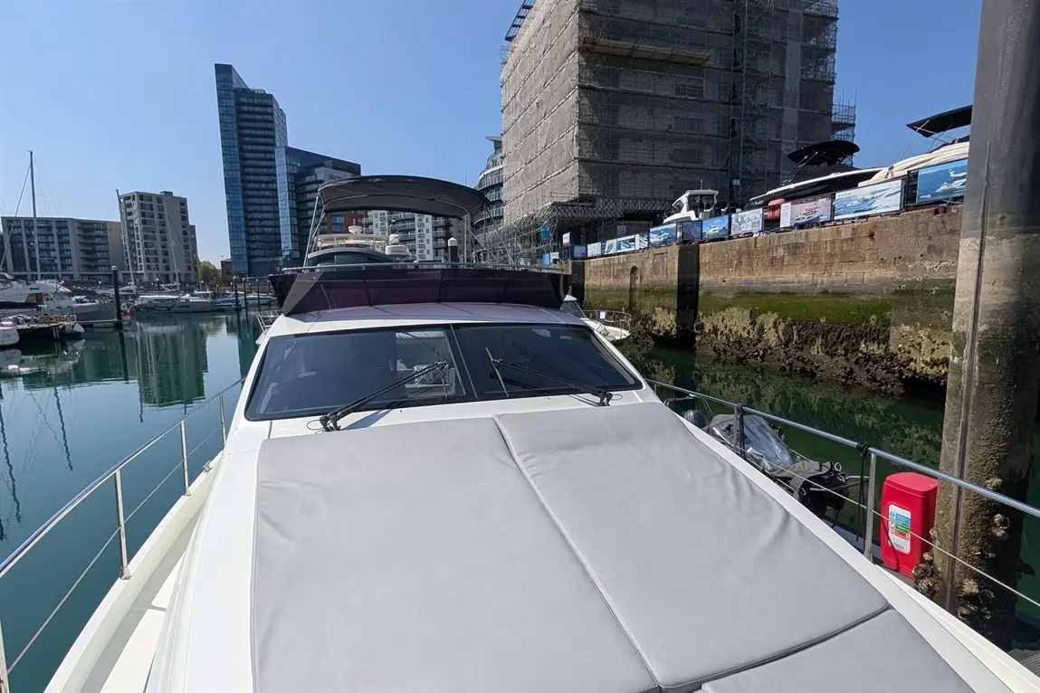 Luxury boat docked in marina, reflecting buildings and clear sky; nearby construction site and other boats visible.