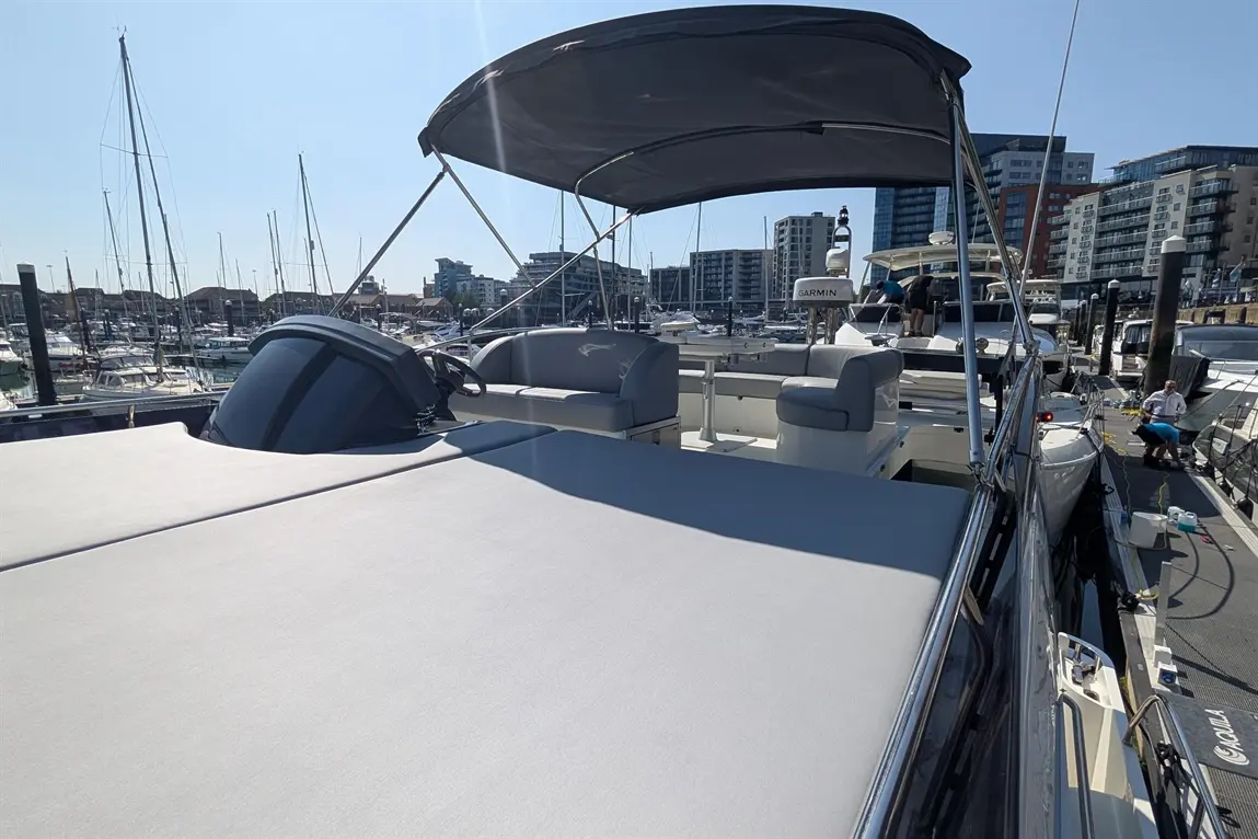 View from a boat's deck showing the steering console and seating, with a marina and modern buildings in the background.