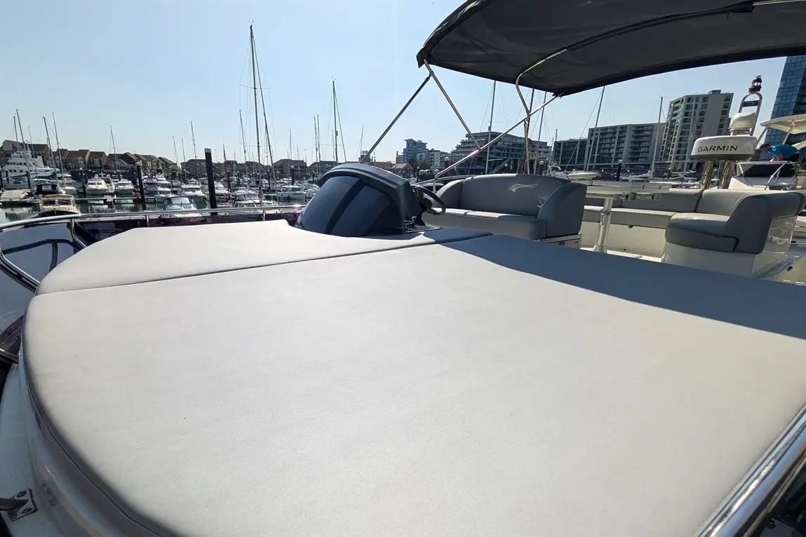Deck of a yacht with a grey sunbed, marina boats in the background, and a Garmin device visible on the console.