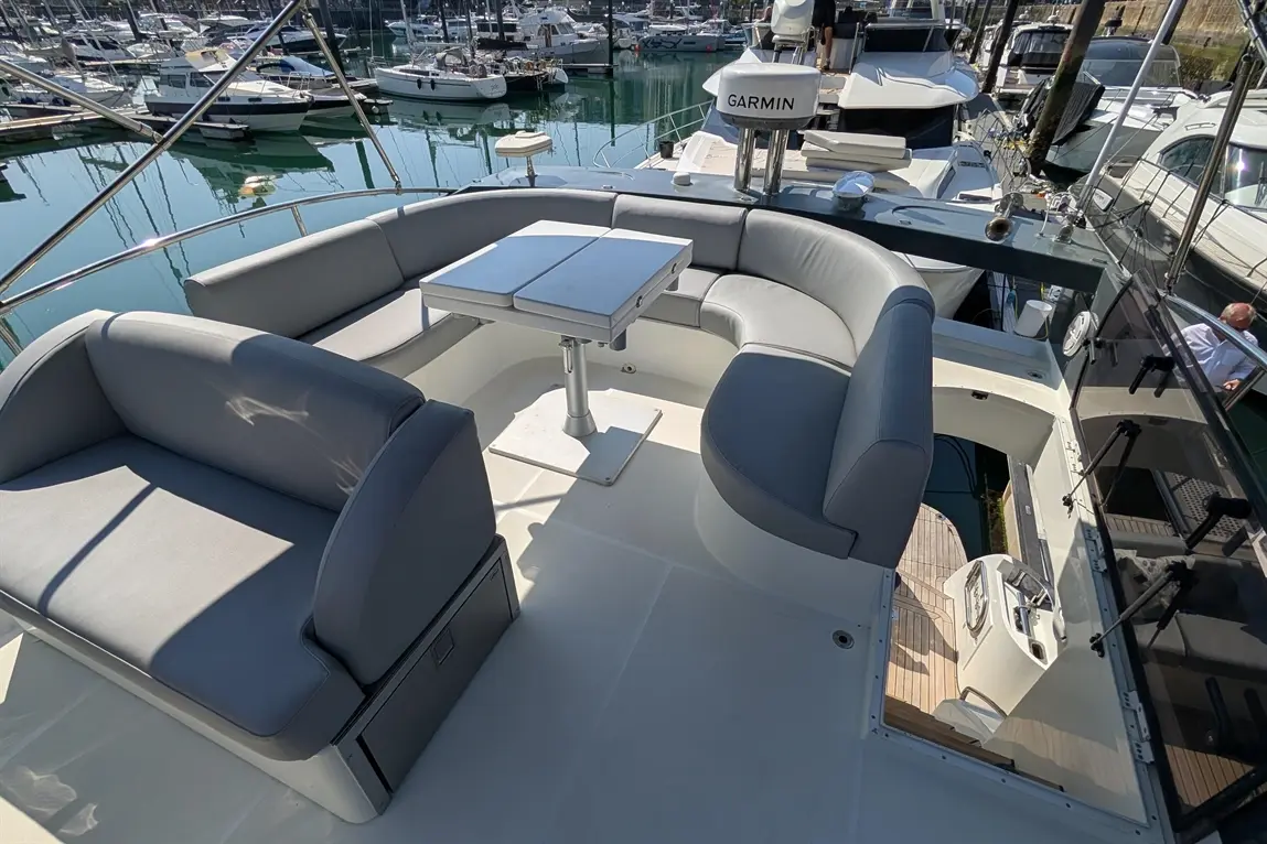 Stylish boat seating area with grey cushions, a foldable table, and marina views, alongside a Garmin navigation device.