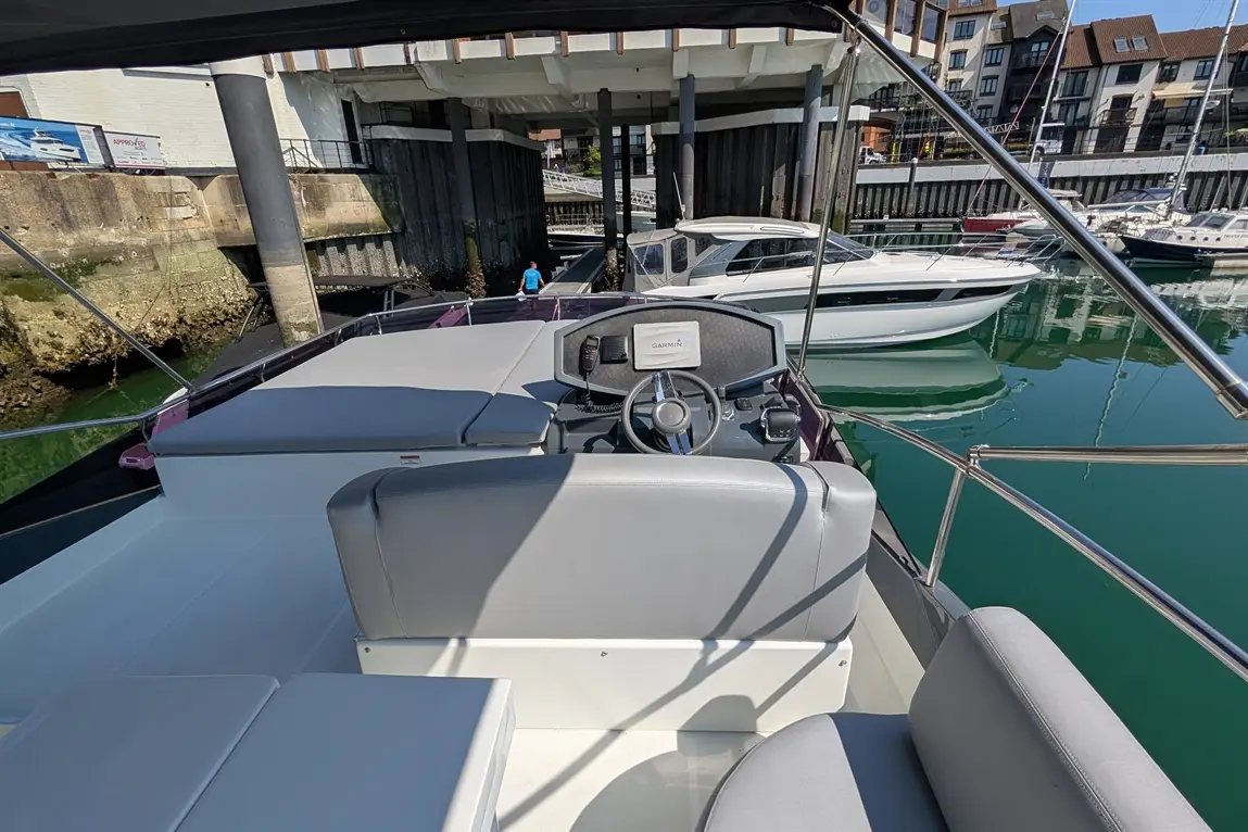 View from the helm of a boat showing a steering wheel, Garmin display, and seating, with docked boats in the background.