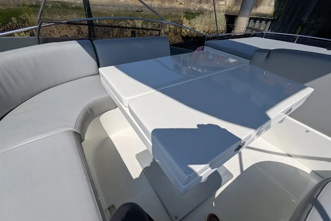 Modern grey boat seating with a white table under sunlight, showcasing a sleek marine design.