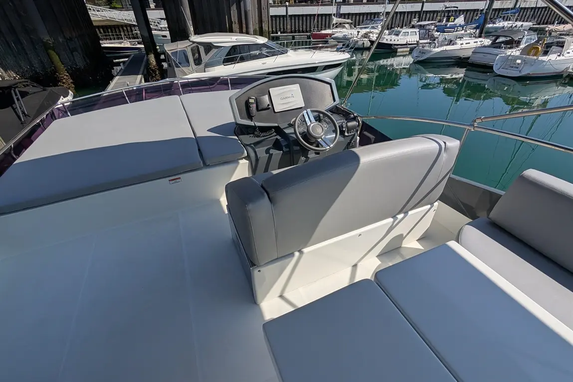 Interior view of a boat cockpit featuring grey seating, a steering wheel, and a Garmin display, with moored boats in the background.