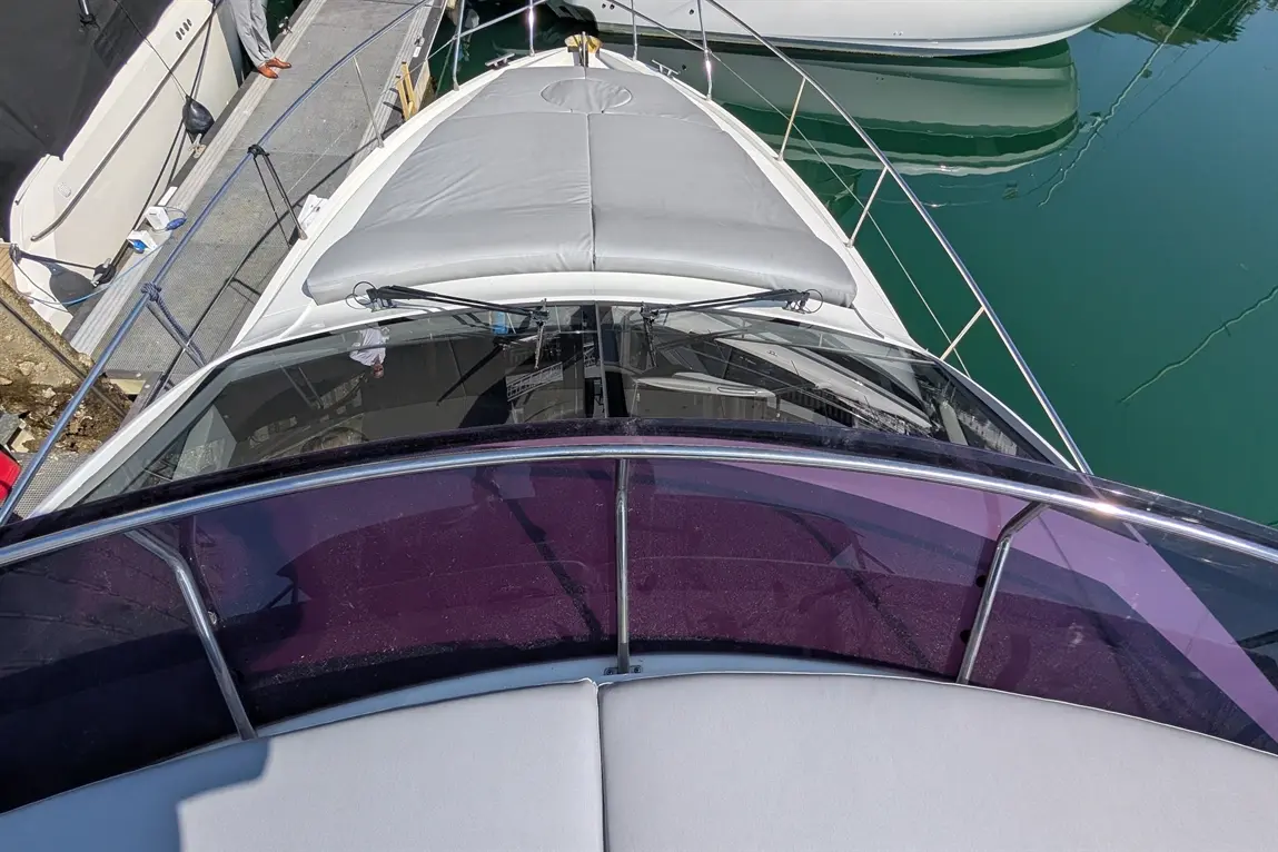 View from above a boat showing a grey deck, purple tinted windscreen, and surrounding boats on calm turquoise water.