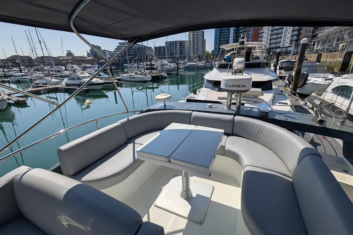 Luxury boat seating with a foldable table overlooking a marina filled with boats and modern buildings in the background.