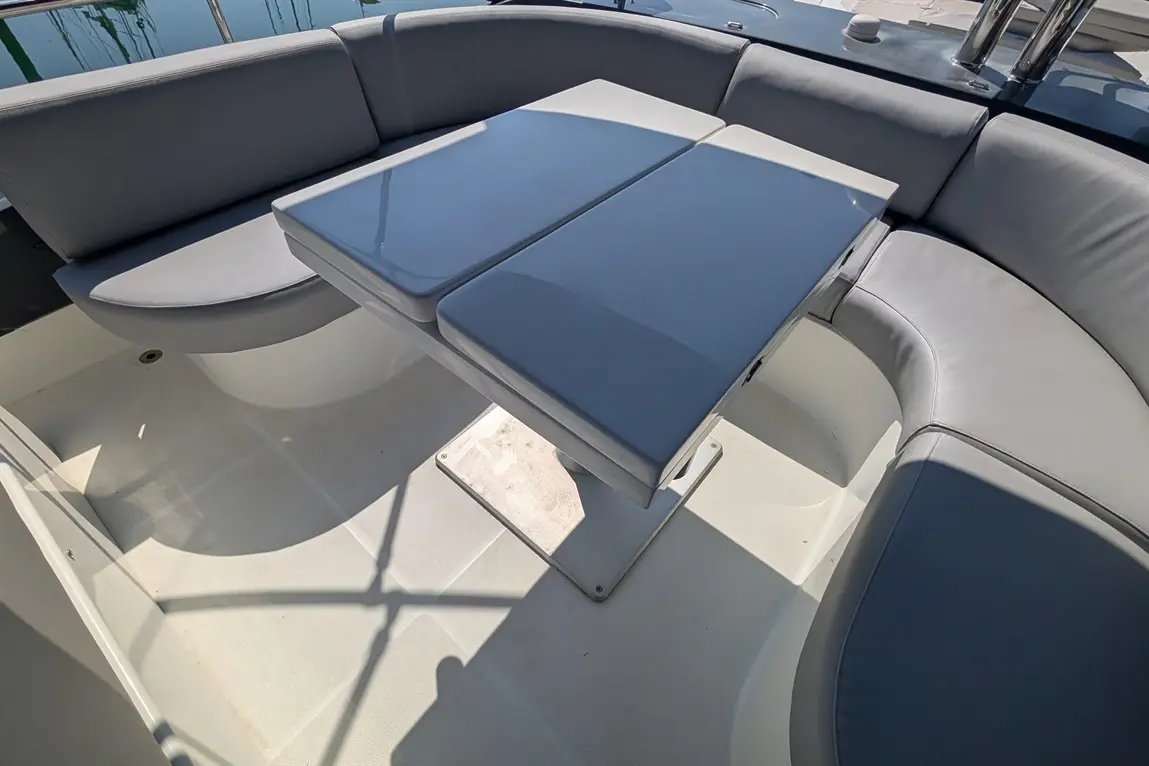 A grey cushioned seating area on a boat featuring a rectangular table, with reflections of water visible in the background.