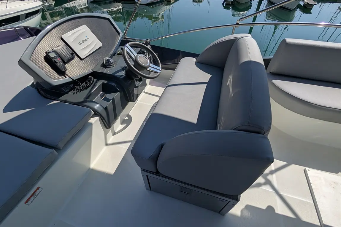 A modern boat cockpit featuring a grey captain's seat, steering wheel, and Garmin display, with calm water and boats in the background.