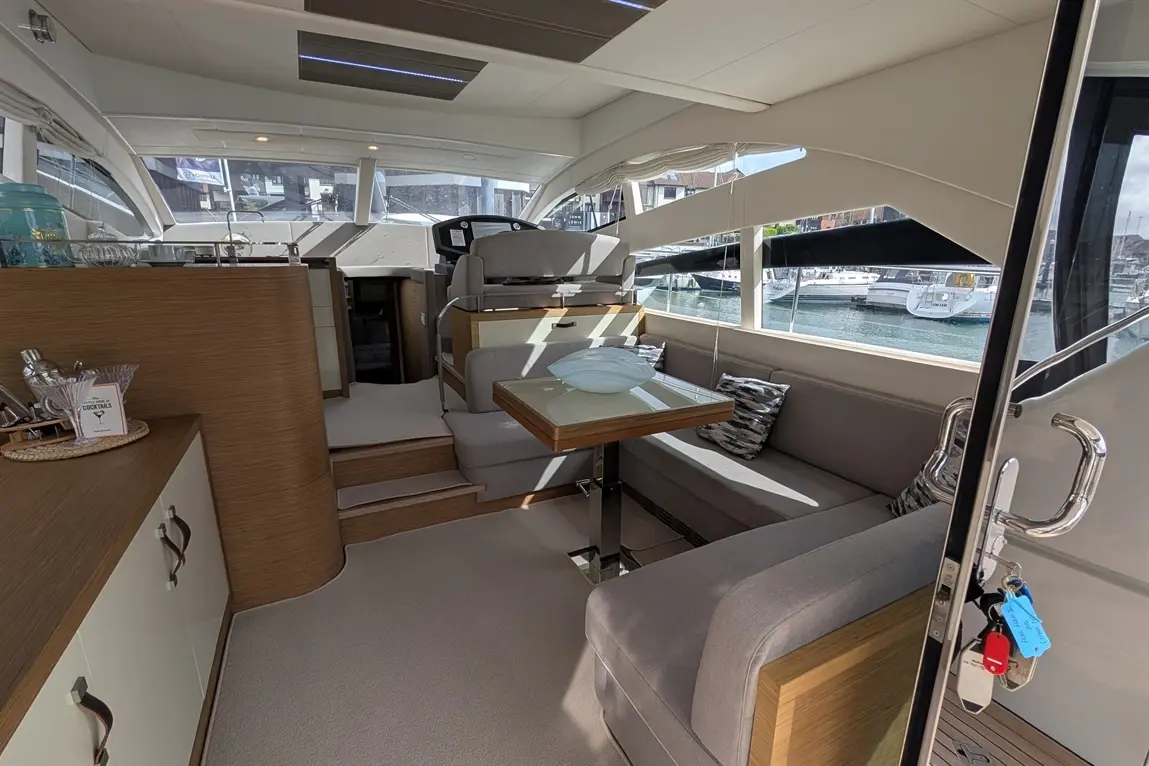 Interior of a luxury yacht showing a lounge area with modern furniture, a dining table, and a view of the marina outside.