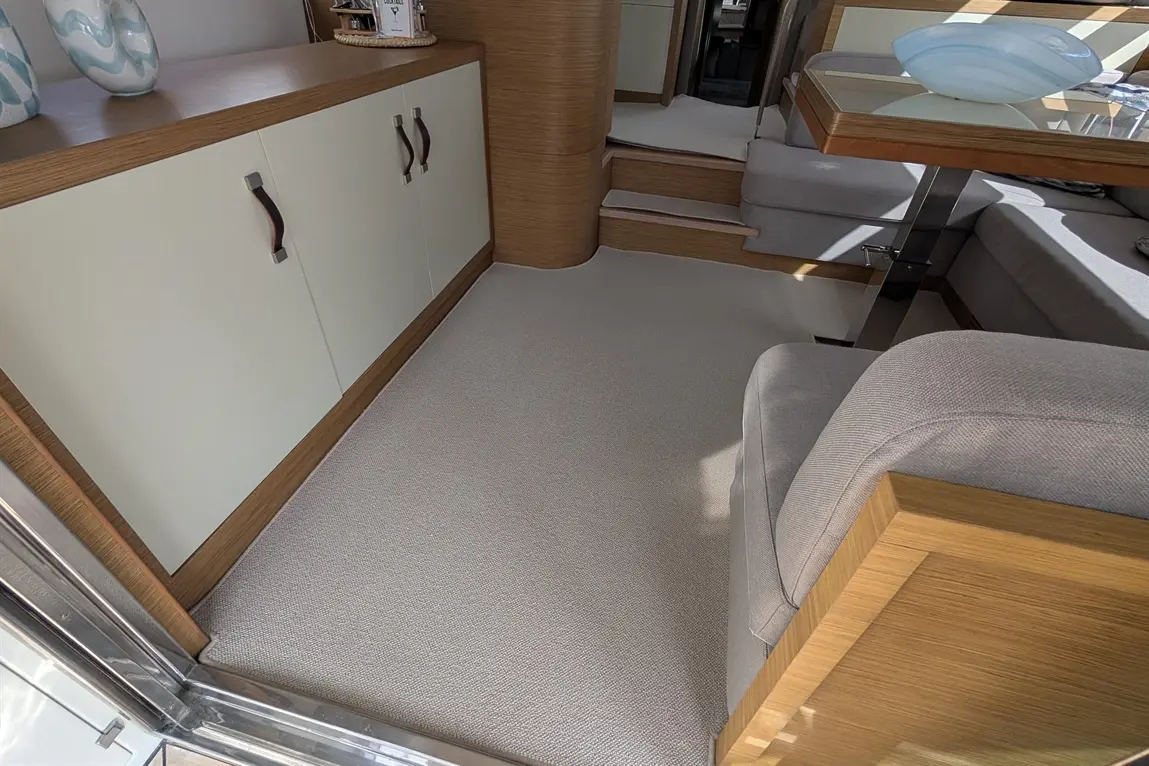 Stylish interior of a yacht featuring a light carpet, wooden furniture, and a glass dining table with a decorative bowl.
