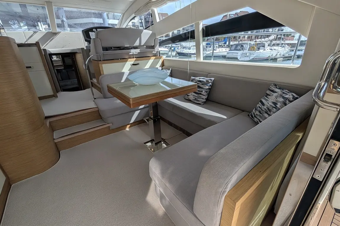 Interior of a yacht featuring a comfortable seating area with a table, decorative vase, and views of moored boats outside.
