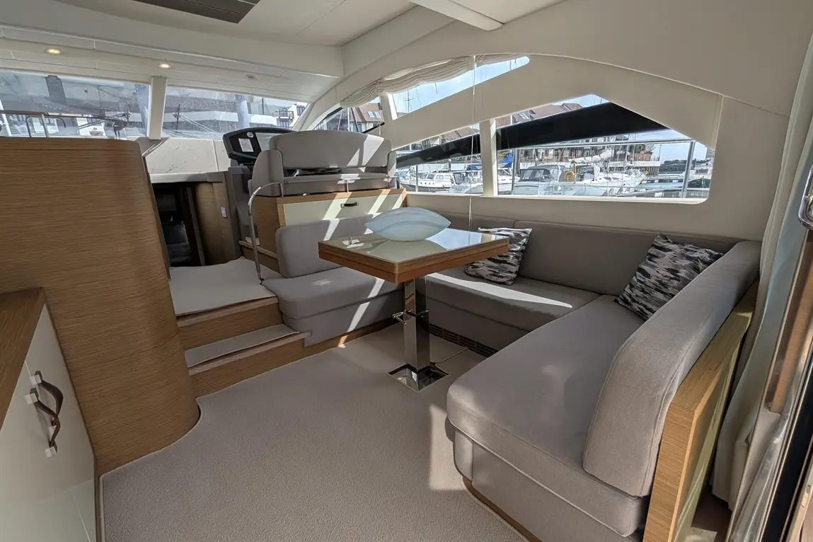 Modern boat interior featuring a dining table, grey seating, and large windows with a view of the marina.