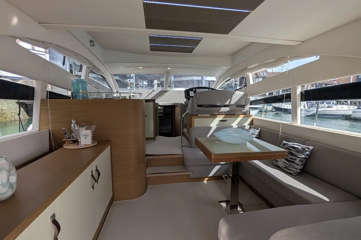 A bright and modern yacht interior featuring a dining table, plush seating, and large windows overlooking a marina.