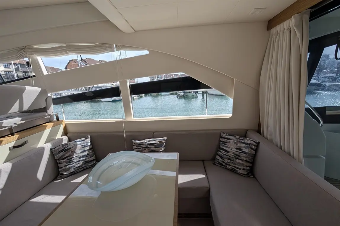 Bright interior of a boat featuring a grey seating area, a glass bowl centerpiece, and a view of the marina through large windows.