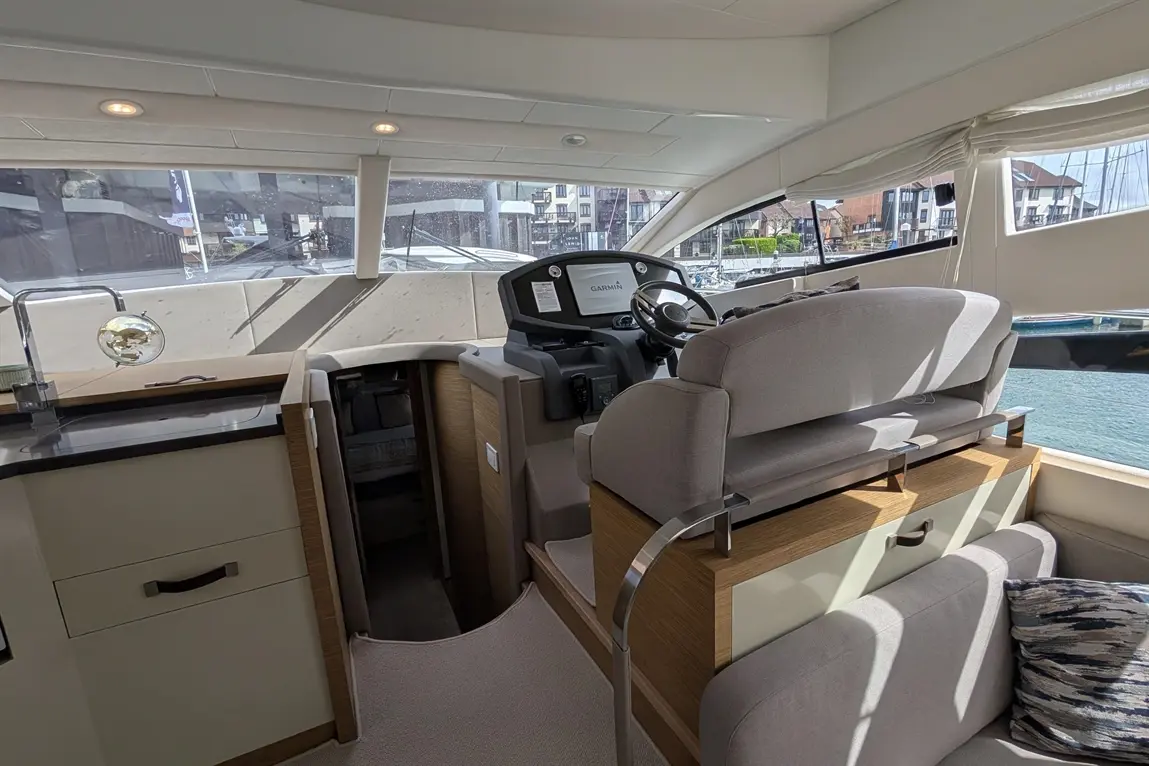 Modern yacht interior featuring a helm station, plush seating, and a scenic view of the marina outside. Garmin display visible.