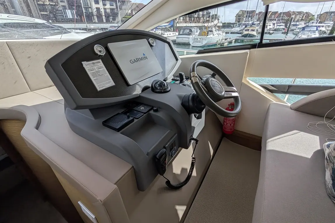 Boat control panel with Garmin display, steering wheel, gauges, and safety equipment in a marina setting.