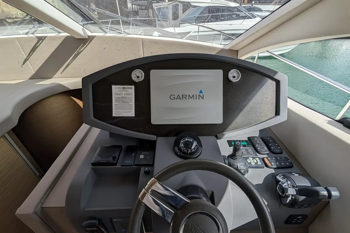 Boat dashboard featuring a Garmin display, steering wheel, controls, and a view of boats in a marina.
