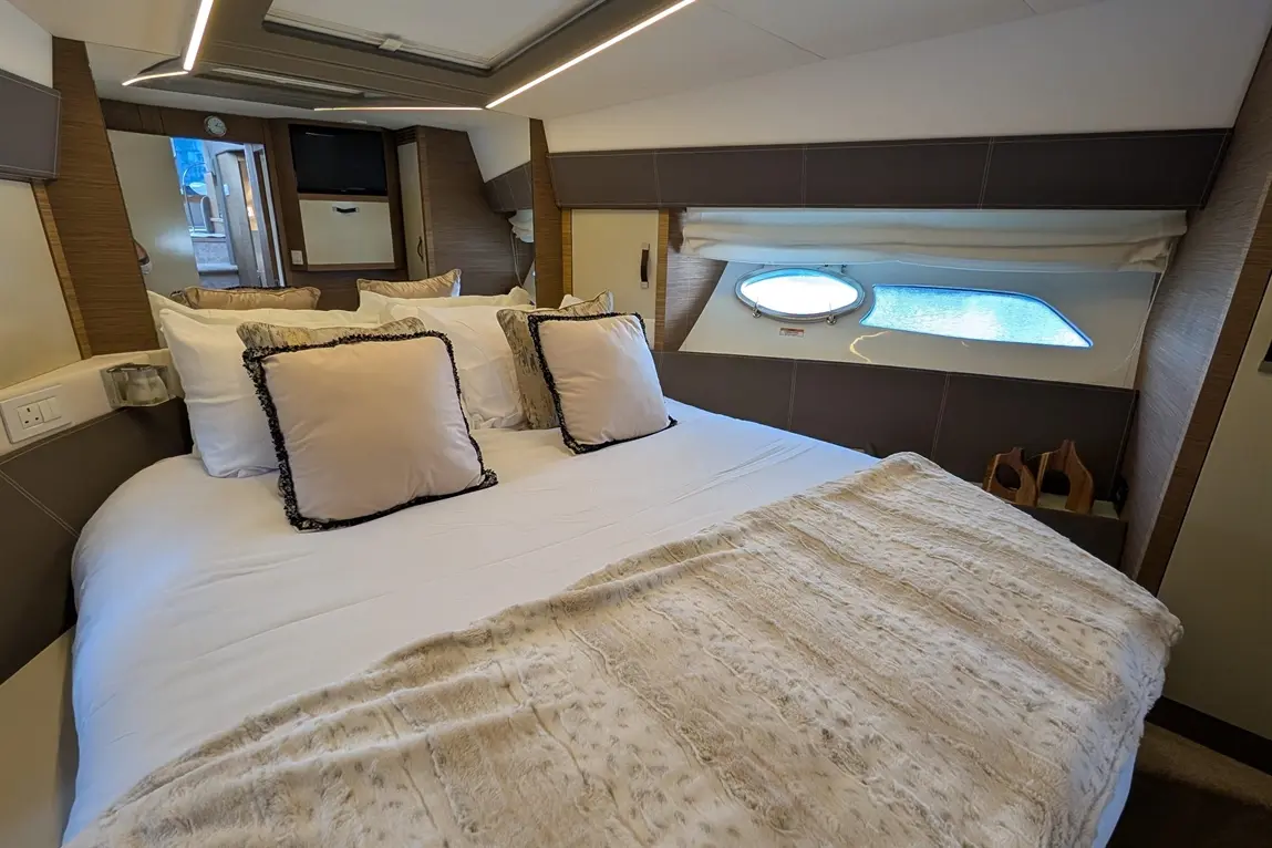Luxurious boat bedroom featuring a double bed with decorative cushions, a faux fur throw, and a porthole window.