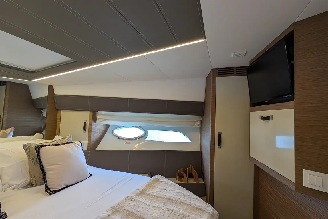 Modern yacht bedroom with a double bed, decorative pillows, a porthole window, and a TV mounted on the wall.