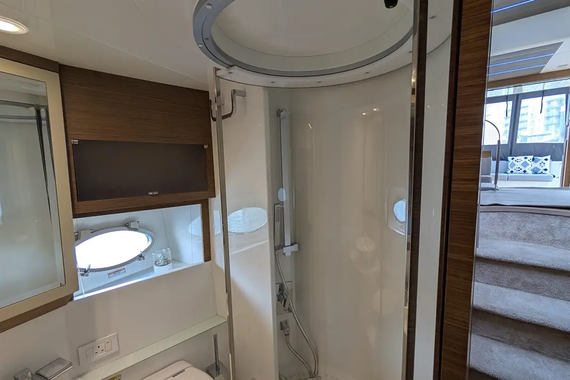 Modern shower enclosure with glass doors, wooden cabinetry, and a small window, leading to a stylish lounge area.