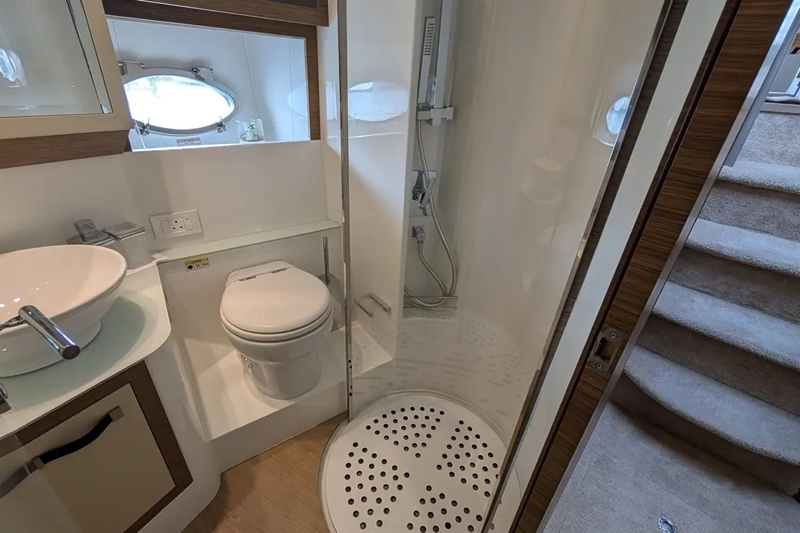 Compact bathroom with a shower enclosure, toilet, and sink, featuring wooden accents and a round window for natural light.