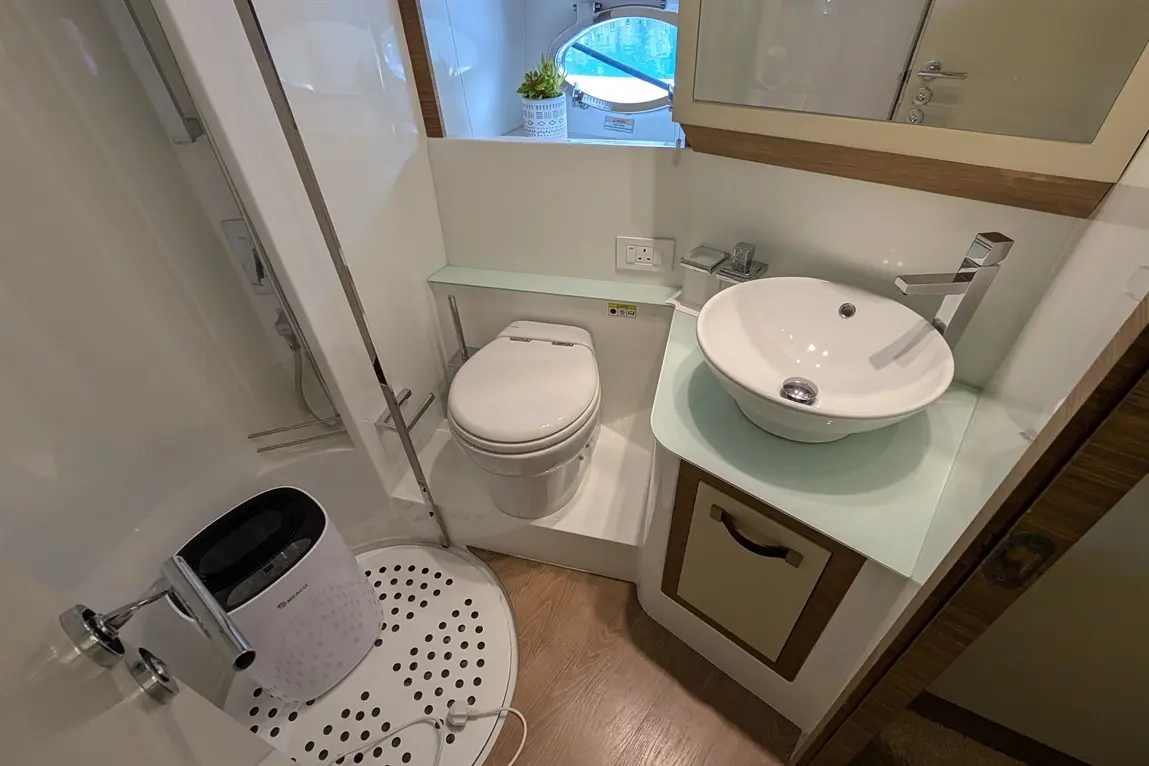 Modern bathroom featuring a shower, toilet, sink, and decor with a small plant by a window, showcasing a clean design.