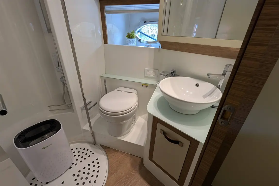 Compact bathroom featuring a shower, toilet, basin, and window with plants, showcasing modern design and cleanliness.